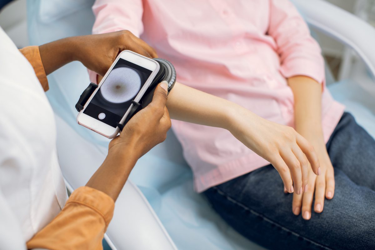 Preventive checkup, skin melanoma days concept. Close up of hands of female doctor dermatologist oncologist holding new generation dermatoscope, examining birthmarks and moles of the patient