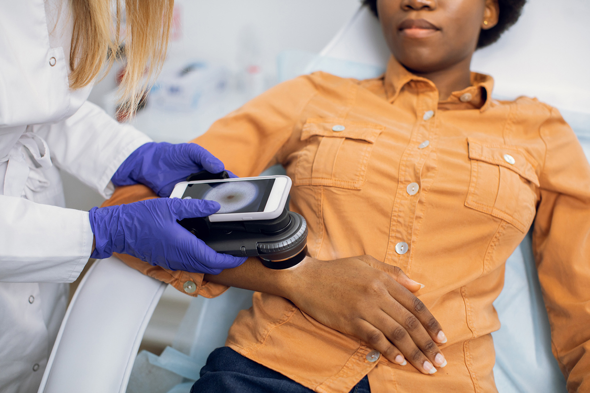 Preventive checkup, skin melanoma days concept. Close up of hands of female doctor dermatologist oncologist holding new generation dermatoscope, examining birthmarks and moles of a woman.