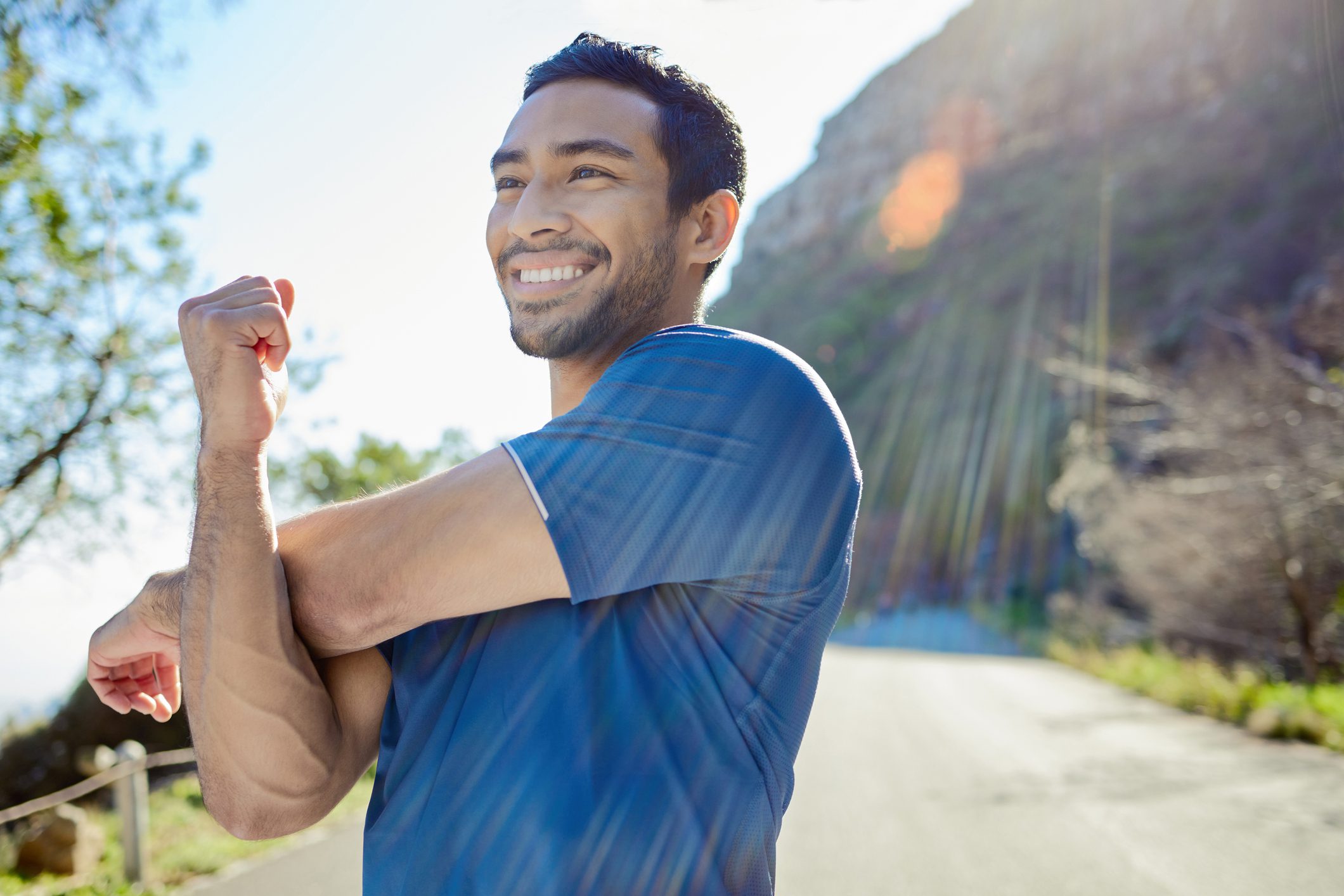 Shot of a young man standing alone and stretching during his outdoor workout